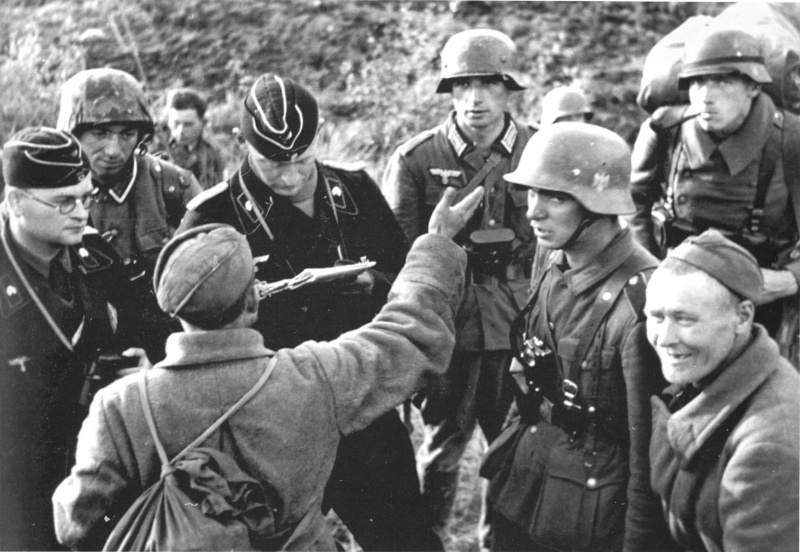 Лейтенант-танкист вермахта допрашивает советского военнопленного. Крайний справа улыбающийся еще один пленный красноармеец.
