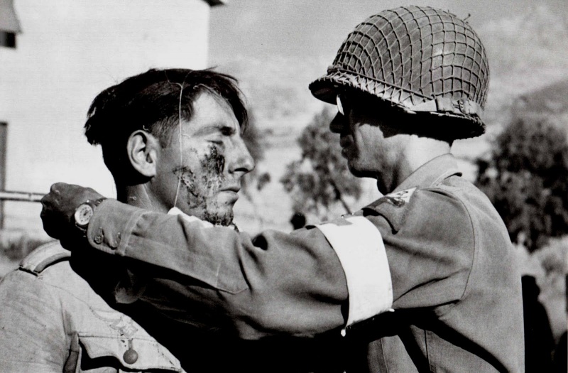 Медик из состава 48-го медицинского батальона 2-й бронетанковой дивизии армии США делает перевязку раненому немецкому солдату.
