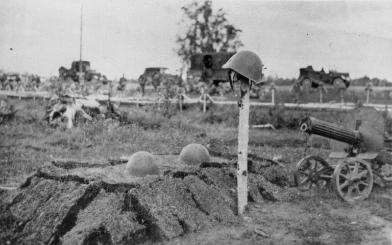 Могила советских солдат (судя по трем советским каскам) и пулемет «Максим». На заднем плане видно еще более десятка могил — уже немецкие (каски на столбиках немецкие).